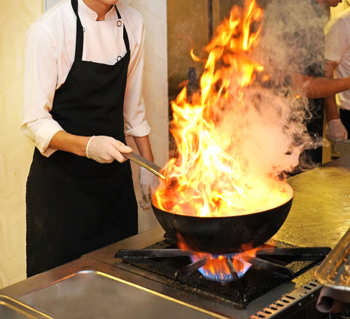 A male Asian Chef cooking vegetables on a wok burner